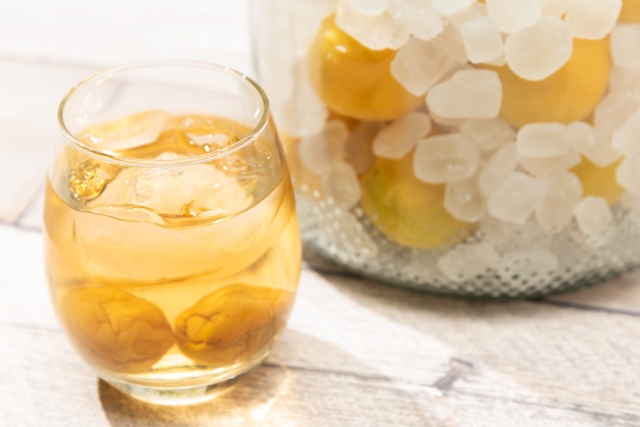 梅の実と角砂糖が入った瓶と側に置かれた梅酒のグラス